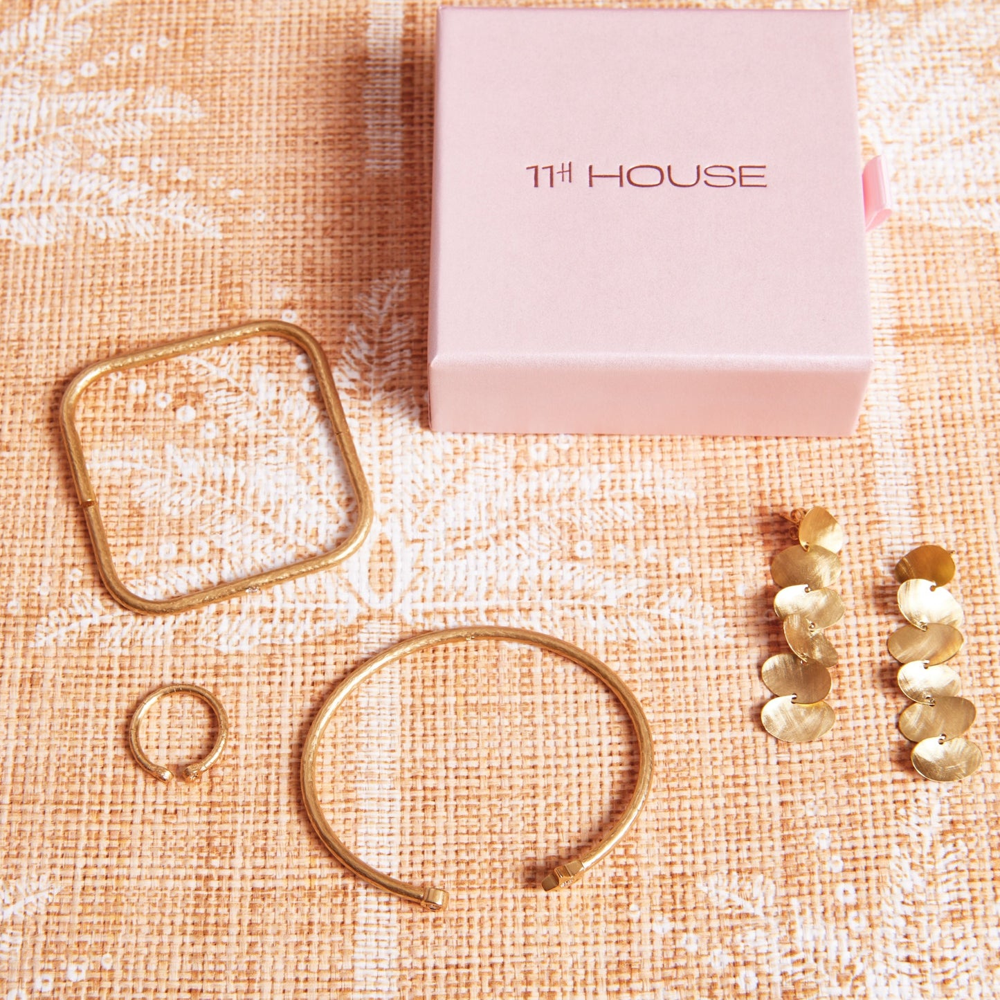 Gold jewelry set on a textured surface with '11th House' branding.