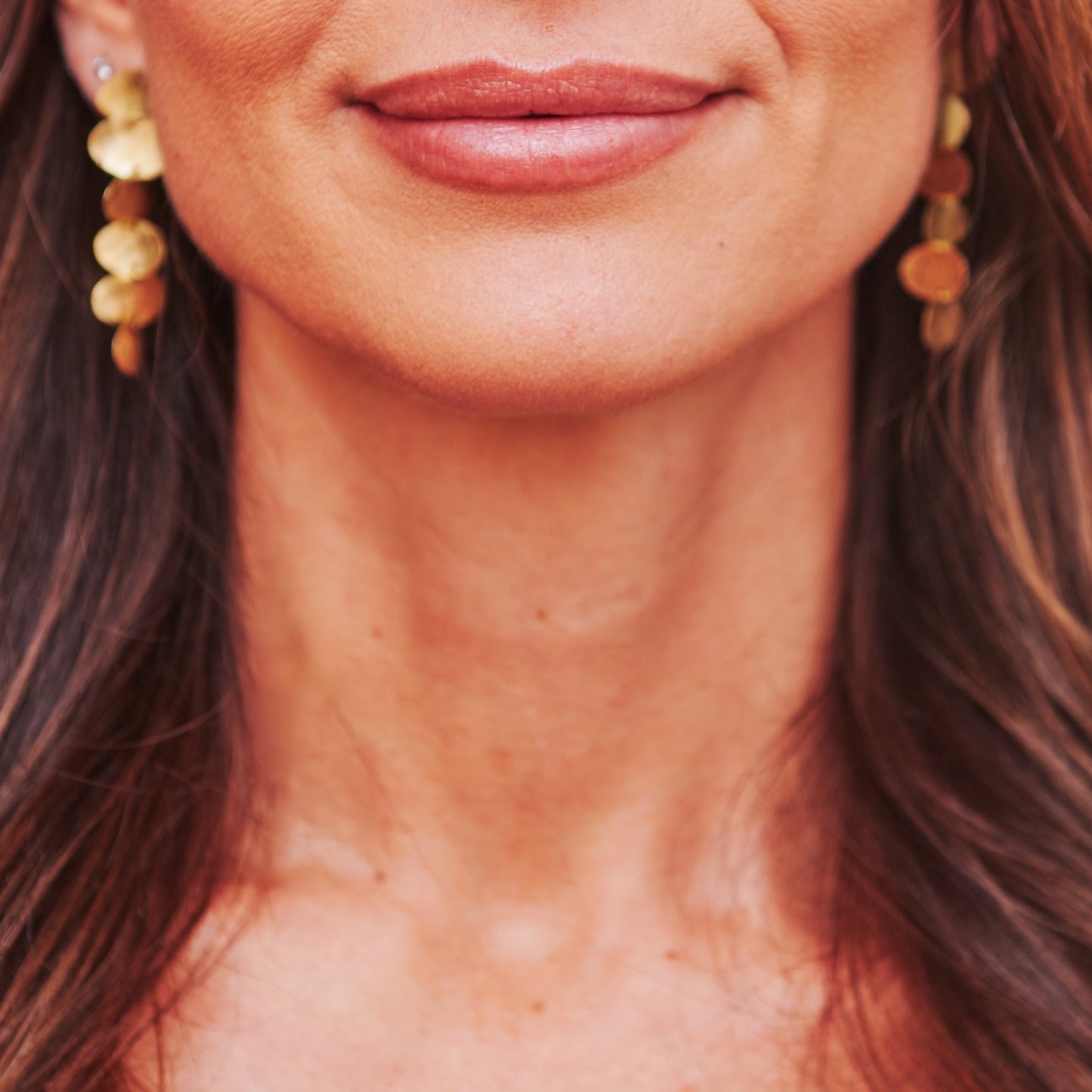 Close-up of a woman with long brown hair wearing gold earrings.